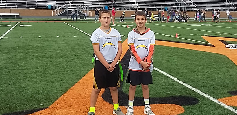 Two youth football players stand side by side on the field.